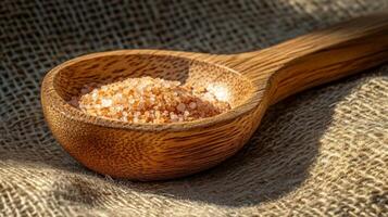 Pink salt rests in a wooden spoon on a rustic cloth in sunlight, highlighting the delicate crystals and natural texture photo