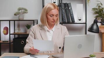 Focused mature freelancer using netbook working with financial graph documents at home office table video