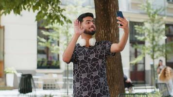 Cheerful man tourist smiling friendly at smartphone camera, waving hands gesturing hello hi greeting video