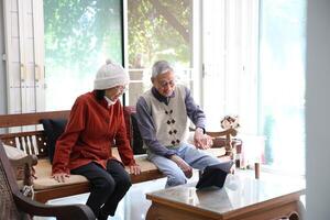 Senior asian couple laughing and sitting on the sofa while watching funny stand up comedy show from streaming digital tablet during winter time for mental health and happiness in marriage photo