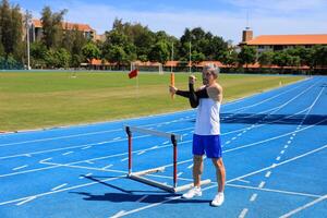 Asian senior athlete is practicing hurdling running in the professional blue track for professional exercise, sport training workout and healthy for longevity concept photo
