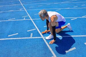 Asian senior athlete is practicing running block start in the professional blue track for professional exercise, sport training workout and healthy for longevity photo