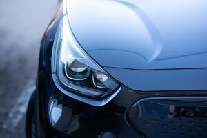 Close-up of a modern car headlight with a sleek, reflective surface. Luxury vehicle front detail with glossy black paint and LED design. photo