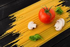 Fresh tomato, mushrooms, and spinach leaves on spaghetti, placed on a black table composition of pasta ingredients. photo