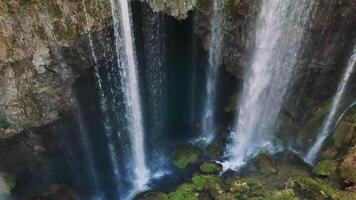 Water plunges from a rocky cliff face, creating a mesmerizing waterfall that flows into a serene pool surrounded by lush green moss in a hidden corner of turkey video