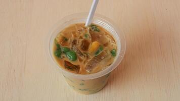 A cup of traditional indonesian iced drink green cendol with brown sugar and coconut milk with a spoon on a wooden table photo