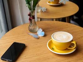 Yellow coffee cup sits on a table next to a cell phone photo