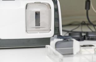 A close-up view of a medical xray scanner with a transparent chamber and various attachments. The background features cables and other equipment, suggesting a clinical setting. photo