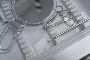 A close-up view of a medical tray containing surgical instruments, including scissors, tweezers, and a mirror, arranged neatly on a white surface. photo