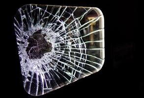 A close-up view of a shattered glass pane with intricate cracks radiating from a central point, set against a dark background. photo