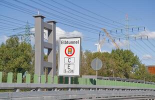 A road sign indicating the Elbtunnel with restrictions for vehicles. The sign shows a bus symbol and specifies operational hours from 5 to 23. In the background, there are power lines photo