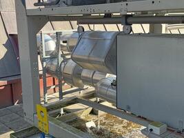 A close-up of industrial piping and equipment on a rooftop. The metallic pipes are connected and appear to be part of a ventilation or HVAC system. The background is a roof. photo