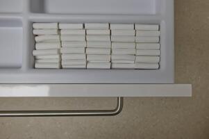 A neatly organized drawer containing rows of white cylindrical cotton rolls for dental use to separate lips from teeth.Neatly Organized Drawer with White Cylindrical Objects photo