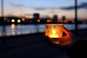 A person holding a candle in front of a river photo