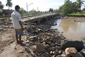 A man stands on a bridge over a river in the middle of a mudslide photo