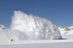 A person riding a snowboard in front of a large snow plow photo