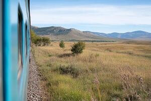 A train traveling through a grassy field with mountains in the background photo