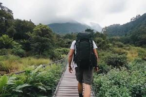 A man with a backpack walking across a wooden bridge photo