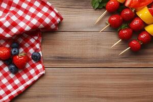 A wooden table with a red and white checkered cloth and a bunch of fruit photo