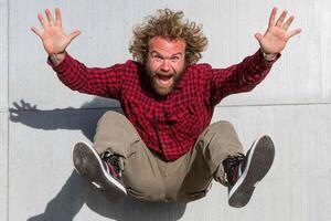 A man with a beard and red shirt is jumping on a skateboard photo