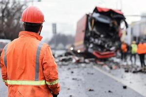 A man in an orange hard hat is looking at a truck that has been destroyed photo