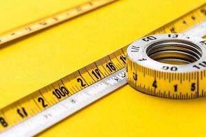 A measuring tape is sitting on top of a yellow surface photo