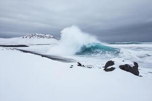 A large wave crashing on the shore of a snowy beach photo