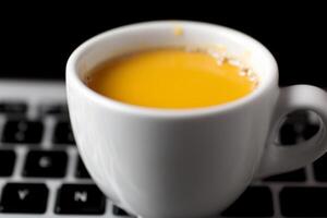 A cup of coffee sits on top of a laptop keyboard photo