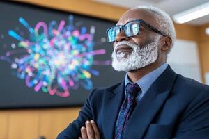 An older man with glasses and a beard standing in front of a projector screen photo