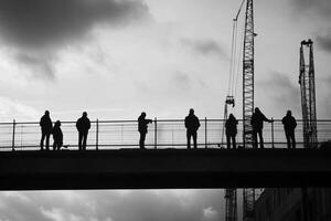 A group of people standing on a bridge with construction cranes in the background photo