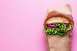 Burger in paper bag on pink background photo