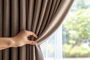A person is opening a curtain to show the window photo