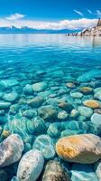 Crystal Clear Waters A Tranquil Lakeside View with Turquoise Water, Smooth Stones, and Distant Mountains Under a Bright Blue Sky for Nature Lovers photo