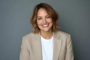 Professional portrait of a smiling woman in a beige blazer against a gray backdrop photo