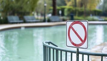 A no swimming sign near a green pool in a park setting. photo