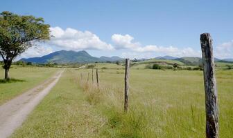 Scenic landscape with a dirt path, fence posts, and mountains in the background. photo