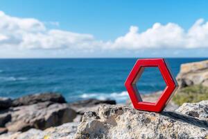 A red hexagonal shape on a rocky shore with ocean in the background. photo