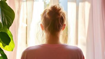 A person with their back to the viewer, gazing out through sheer curtains. photo