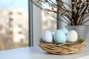 A decorative nest with pastel-colored eggs on a table by a window. photo