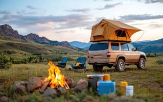 Rustic camping setup with a campfire and rooftop tent in a serene mountainous landscape during dusk photo