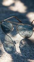 Broken sunglasses casting shadows on a textured surface under soft lighting photo