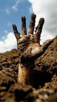 Human hand reaching out from dark, muddy soil under dramatic sky photo