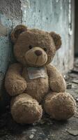 Abandoned teddy bear sitting against a worn-out wall in a derelict room photo