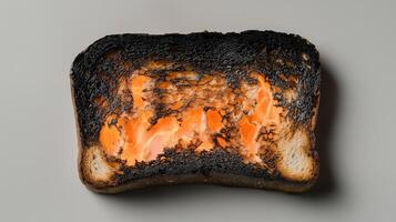 Burnt toast slice with charred crust and orange center on gray background photo