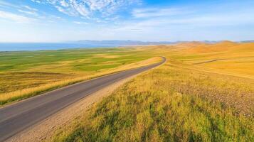 Winding road through vast yellow and green fields under a blue sky with clouds photo