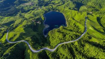 Aerial view of serpentine road by a scenic lake surrounded by lush green hills photo