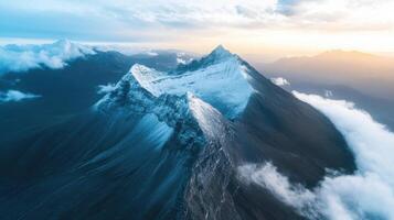 Aerial view of snow covered mountain peak surrounded by misty clouds at sunrise photo