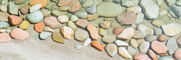 Colorful pebbles and clear water along the sandy shoreline of a calm beach photo