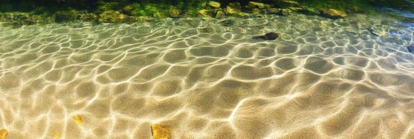 Sunlit waters with ripple patterns on clear shallow riverbed and rocks photo