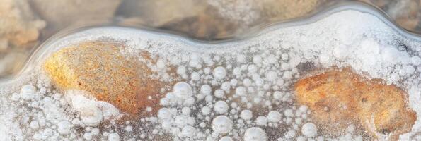 Frozen river surface with ice bubbles and submerged rocks in winter season photo